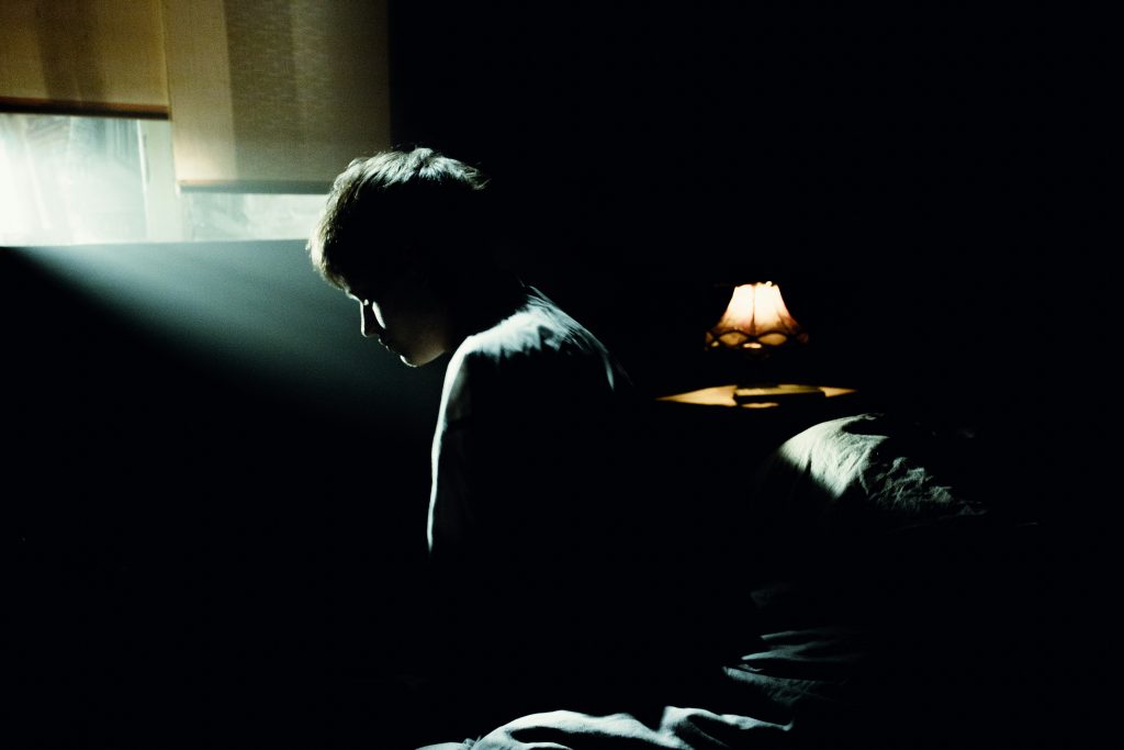 Man reflecting on morning routine in low-lit bedroom, beginning to understand how to build self control.