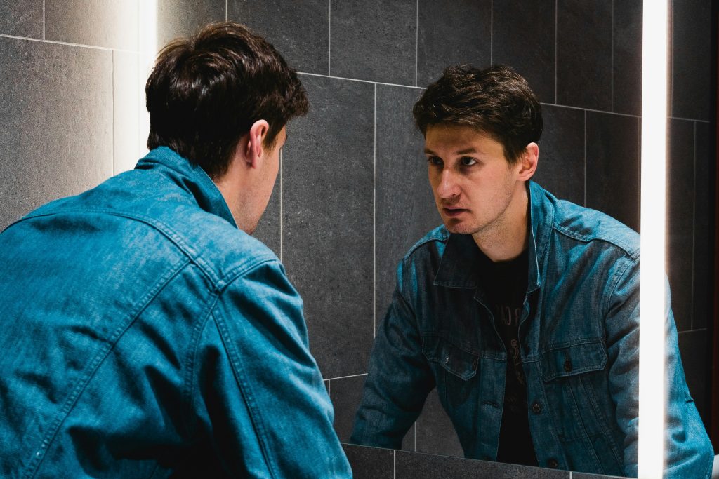 Man frustrated with gym progress while staring into mirror.
