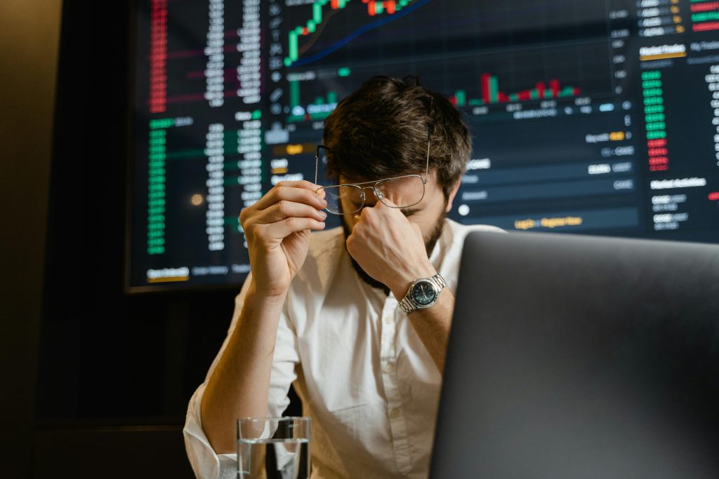 Frustrated man holding head in hands in front of multiple digital screens.