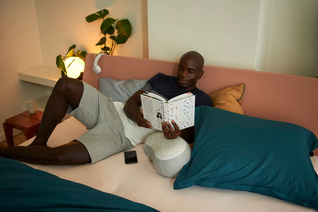 Man completing his daily routine for men with a book, soft lighting, and phone turned off beside him.